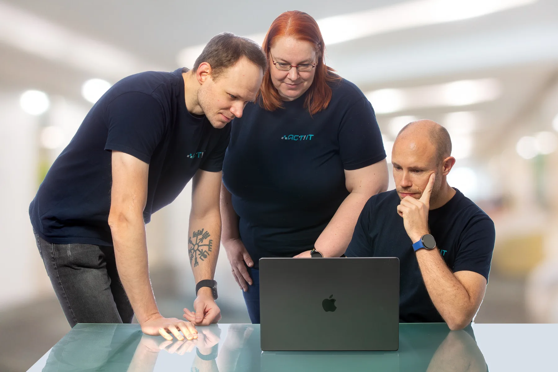 Drei Personen des ACT! IT Teams an einem Tisch vor einem Laptop